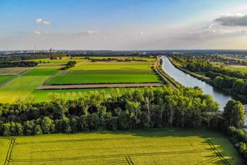 Aerial view of green farmland and river under a clear blue sky, showcasing vibrant agricultural landscapes.